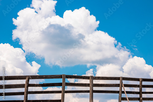 Blue sky and white fluffy clouds behind the wooden fence