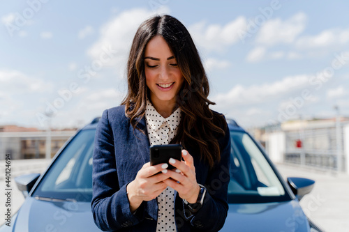 Smiling businesswoman using smart phone by car photo