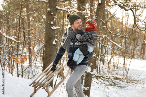 Father with sled holding son while walking in snow during winter photo