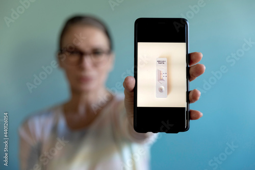 Woman showing photograph of corona rapid test kit on mobile phone photo