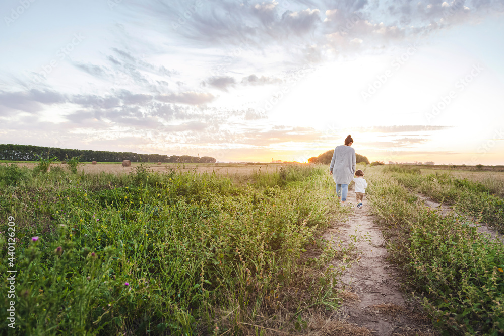 Mother walking with baby son along countryside dirt road at sunset Mother walking with baby son along countryside dirt road at sunset