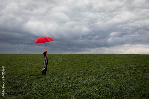 Carefree woman with red umbrella standing in agricultural field during stormy weather photo