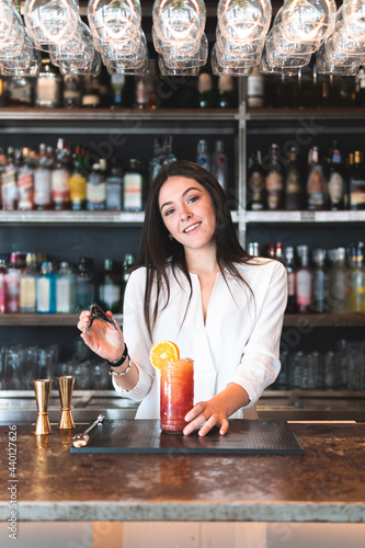 Smiling beautiful female bartender holding serving tong at bar counter photo