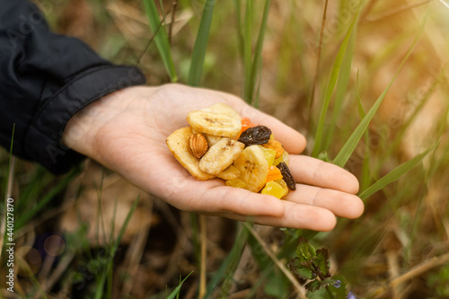 Different dried fruits, nuts in a female hand on a background of green grass. Snack during the hike, walk. Healthy vegetarian food.