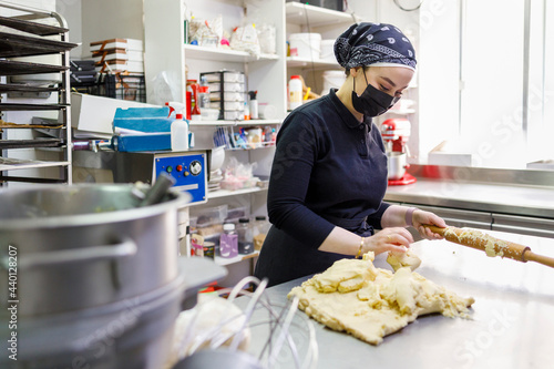 Female baker with rolling pin and dough in commercial kitchen at bakery photo