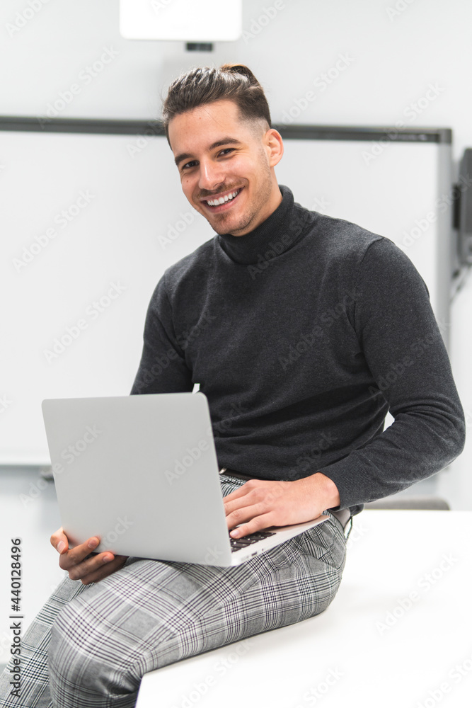Young businessman with laptop sitting on table in board room at office Young businessman with laptop sitting on table in board room at office