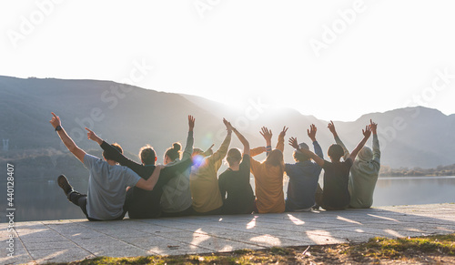 Cheerful male and female friends sitting together on promenade during sunny day