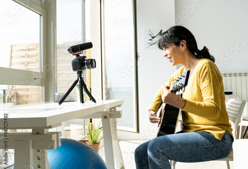 Maturewoman vlogging while playing guitar at home photo