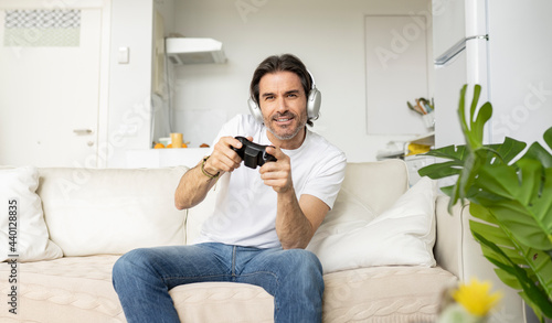 Excited man playing video game while sitting on sofa in living room photo