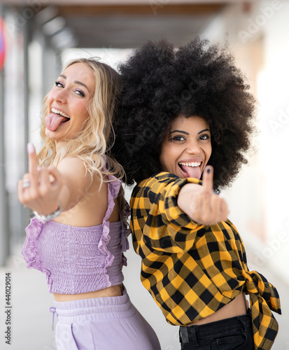 Multi-ethnic female friends sticking out tongue while showing middle finger