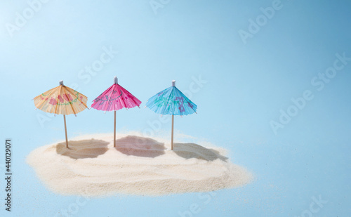 Three colorful umbrellas on the island of sand in the sunshine  a summer beach vacation and travel concept.