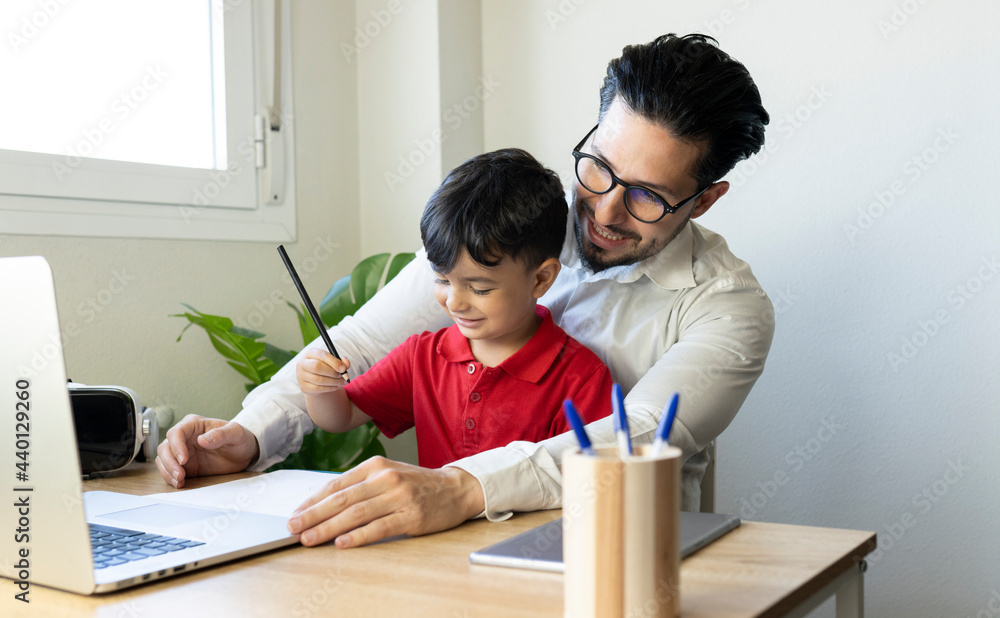 Businessman looking at laptop while sitting with son at home Businessman looking at laptop while sitting with son at home