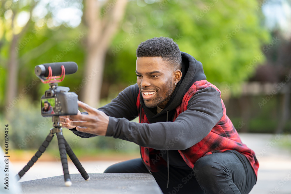 Smiling male vlogger adjusting camera on tripod at public park Smiling male vlogger adjusting camera on tripod at public park