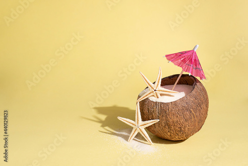 Fotografía Coconut with starfish, sand and umbrella on yellow background in bright sunlight, summer travel concept
