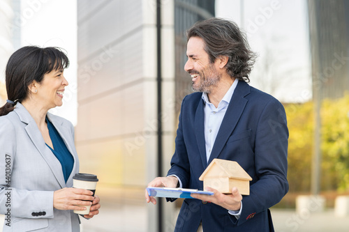 Smiling male real estate agent with house model discussing with female customer holding disposable cup in park photo