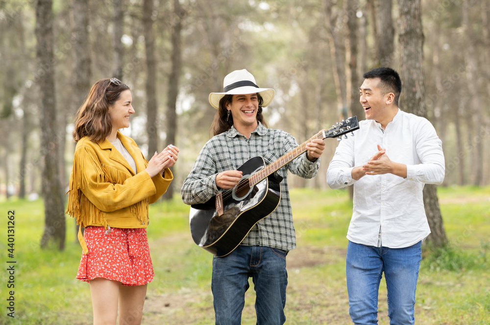 Man with male and female friends playing guitar in forest Man with male and female friends playing guitar in forest