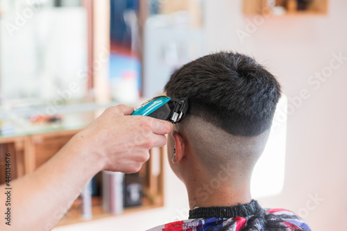 Male hairdresser using machine to do hairstyle of teenage boy at barber shop photo