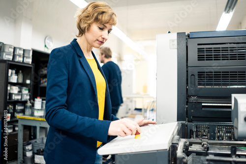 Female engineer using printing machine while working with colleague in industry photo