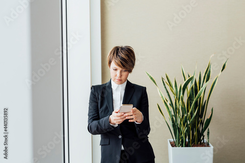 Businesswoman using mobile phone by potted plant in office