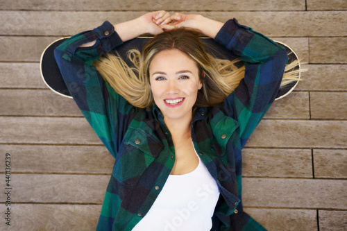 Smiling woman with arms raised lying on skateboard photo