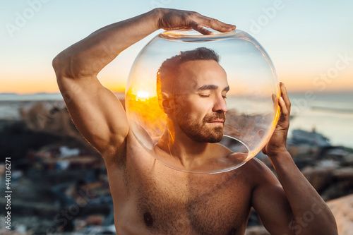 Handsome shirtless man seen through glass bowl during sunrise photo