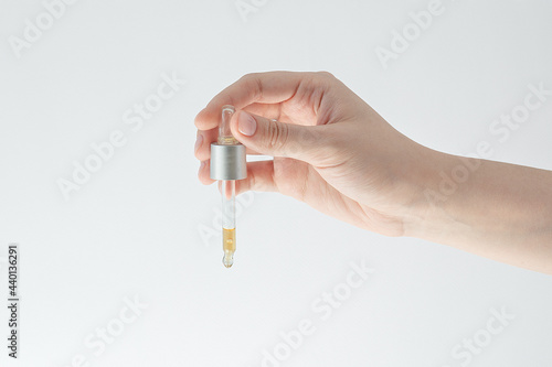 beautiful female hand holds a dropper with a cosmetic product on a white background, the concept of facial and body skin care, moisturizing, anti-wrinkle product