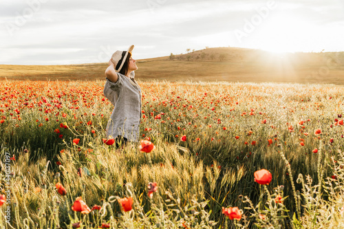 Mid adult woman wearing hat standing in poppy field during sunny day photo