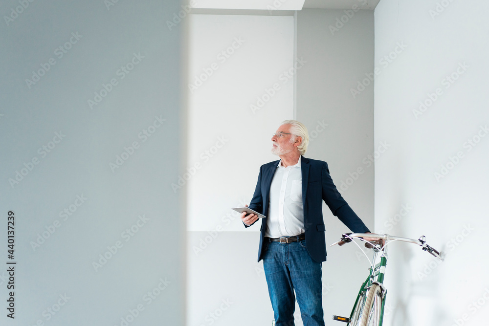Senior male professional looking away while standing near bicycle at office Senior male professional looking away while standing near bicycle at office