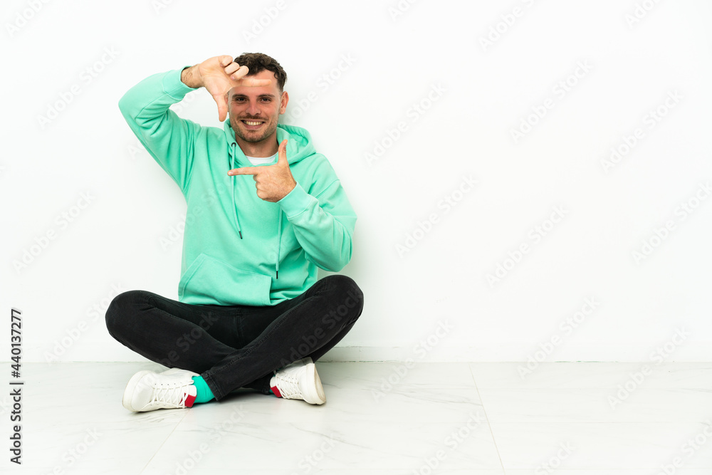 Fototapeta premium Young handsome caucasian man sitting on the floor focusing face. Framing symbol