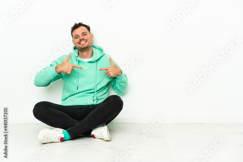 Young handsome caucasian man sitting on the floor proud and self-satisfied