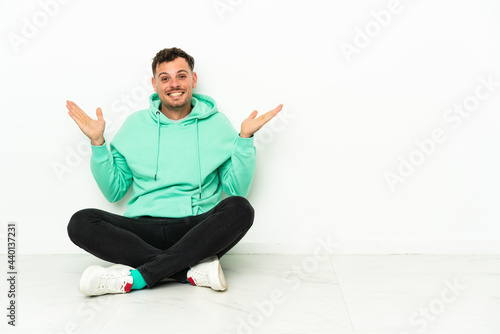 Young handsome caucasian man sitting on the floor with shocked facial expression