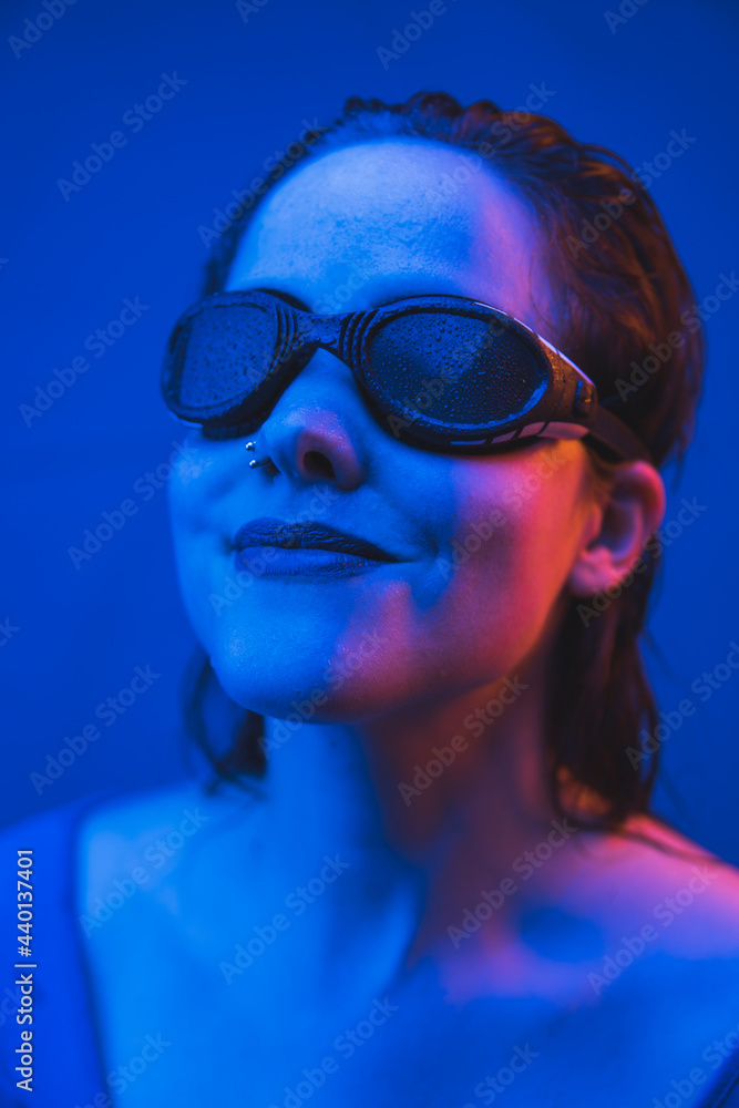 Beautiful woman wearing swimming goggles in front of blue background Beautiful woman wearing swimming goggles in front of blue background