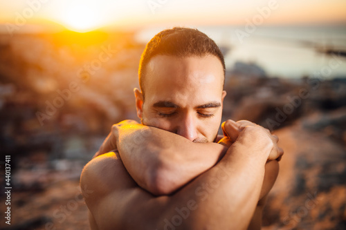 Shirtless man with eyes closed hugging self during sunrise photo
