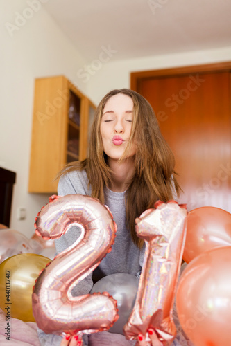 Young woman puckering while holding number 21 balloons in bedroom at home photo