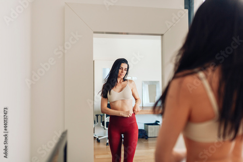 Woman looking in mirror while adjusting pants in living room at home photo