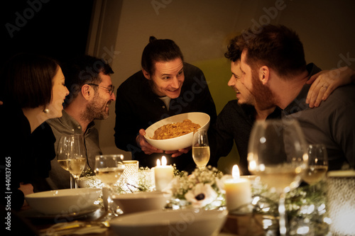 Smiling man offering pasta to male and female friends at home photo