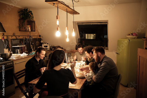 Male and female friends eating pasta at dining table in kitchen photo