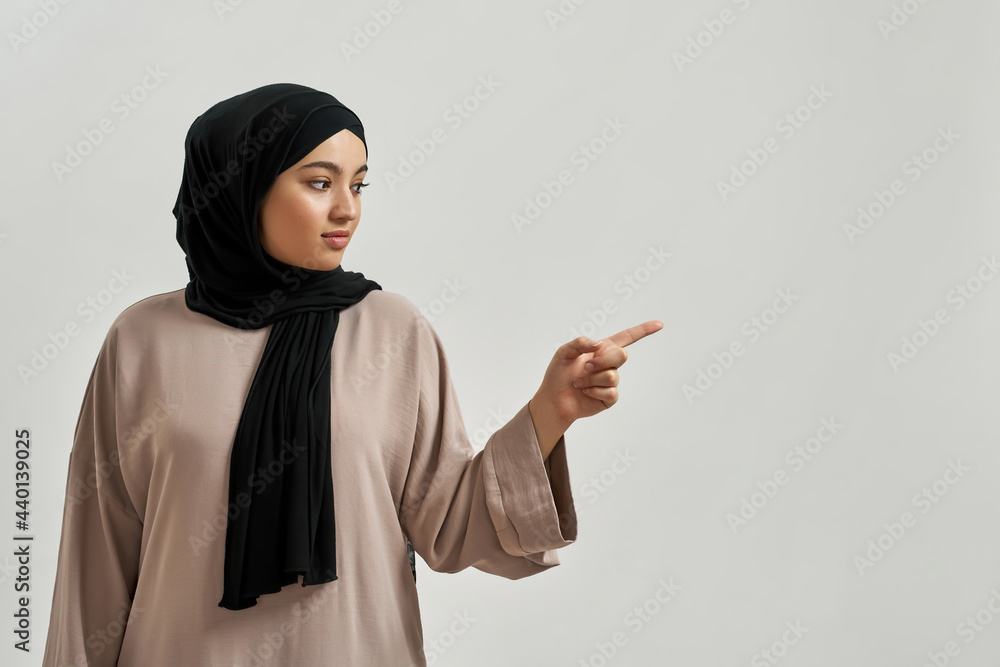 Cheerful young arabic woman in hijab pointing to side Cheerful young arabic woman in hijab pointing to side