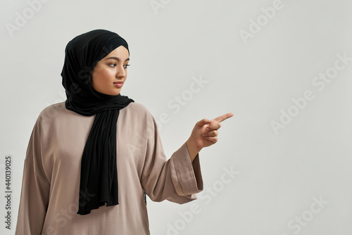 Photography Cheerful young arabic woman in hijab pointing to side