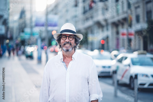 Portrait of attractive senior man with white clothing and hat posing at camera in street of Madrid