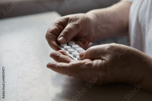 Sad old woman taking pills, health problems in old age, expensive medications. An elderly woman's hands unpacking several pills for taking medication. Grandma takes tablet and drinks a glass of water