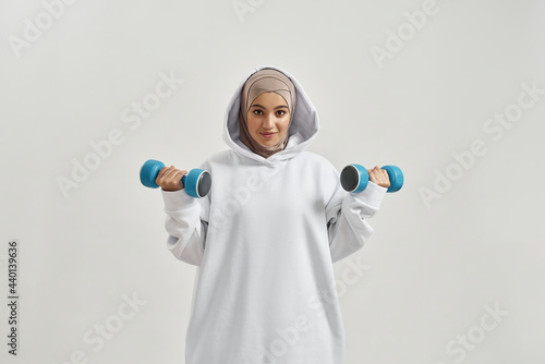 Beautiful young arabian girl in hijab lifting dumbbells