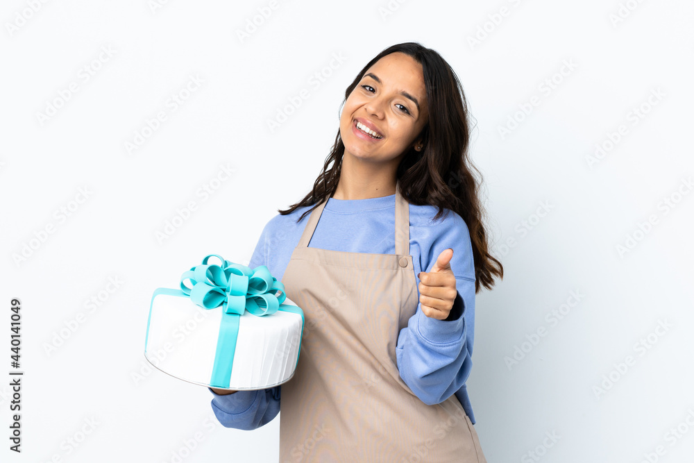 Pastry chef holding a big cake over isolated white background with thumbs up because something good has happened Pastry chef holding a big cake over isolated white background with thumbs up because something good has happened