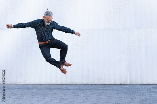 Mature man looking down while jumping on footpath
