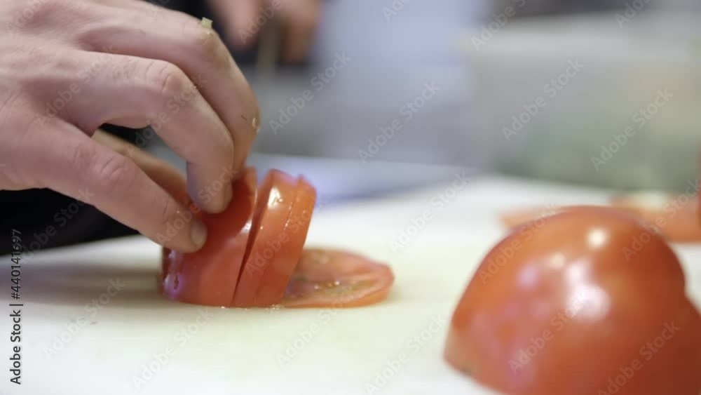 Cook hand cutting tomato. Close up shot of chef's hands cutting a fresh red tomato with knife on board Cook hand cutting tomato. Close up shot of chef's hands cutting a fresh red tomato with knife on board