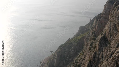 Aerial top shooting over amazing sea with sun glare and high cliff mountains at summer sunset amazing view. Shooting from helicopter beautiful nature scenery rocky landscape with coastline seascape photo