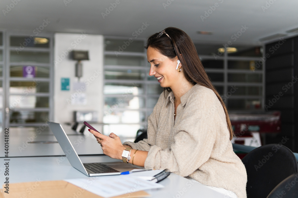 Smiling young businesswoman using smart phone at desk in office Smiling young businesswoman using smart phone at desk in office