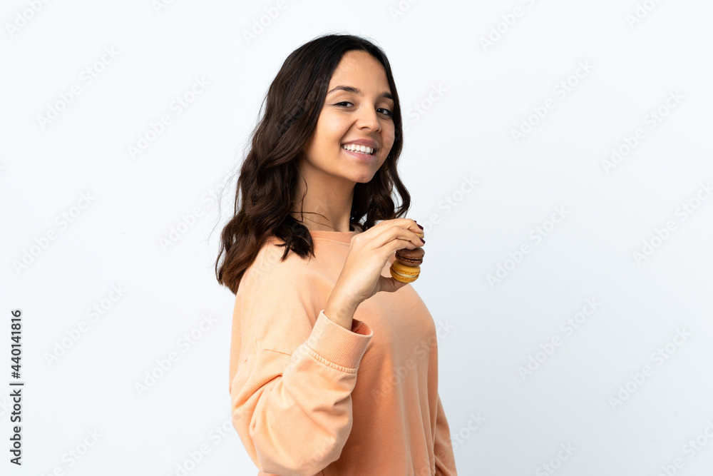Young woman over isolated white background holding colorful French macarons and pointing it Young woman over isolated white background holding colorful French macarons and pointing it