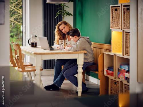 Mother teaching son at home in front of laptop at home photo