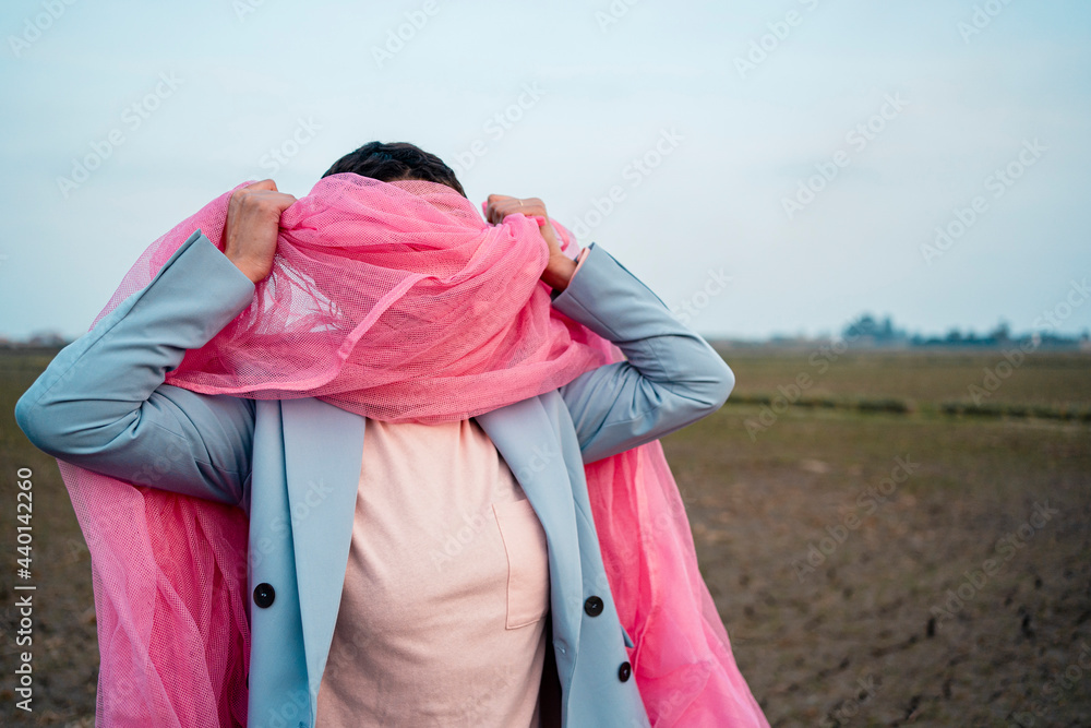 Young woman covering face with pink tulle net in front of sky Young woman covering face with pink tulle net in front of sky